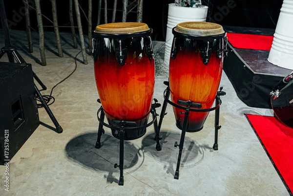 Fototapeta A pair of glossy red-orange gradient conga drums on black stands, positioned on stage, ready for a live performance with rich acoustic rhythms