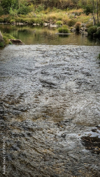 Fototapeta Clear waters of the Tinhela River at Praia Fluvial Rebelos in Murça, Trás-os-Montes, Portugal. A scenic tributary of the Tua, surrounded by green banks, invites nature lovers to relax and explore.