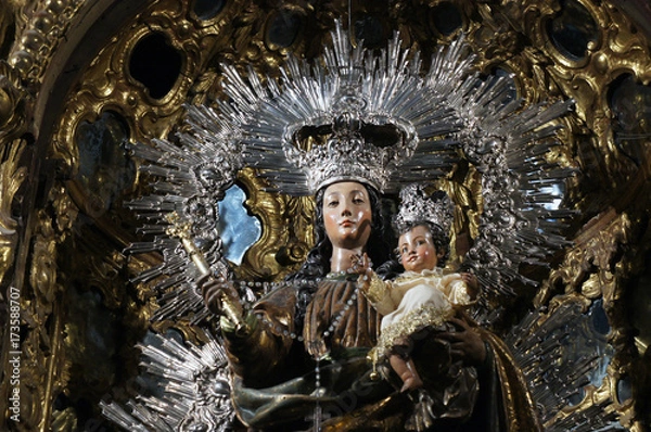 Fototapeta Close-up of traditional procession statue of Madonna and the Child in church of Sevilla, dressed in black, white and silver with some baroque ornaments in behind