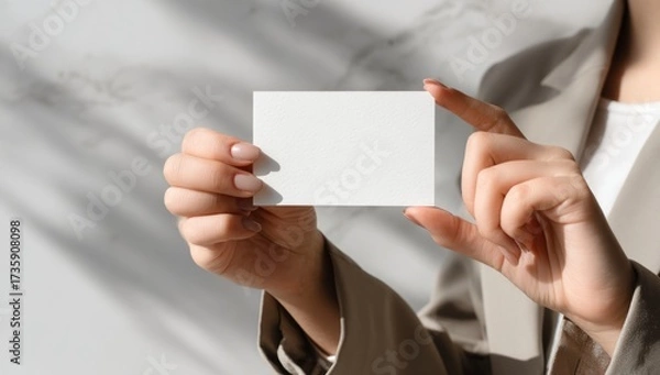 Fototapeta Womans hands holding a blank white business card with natural light and shadow overlay.