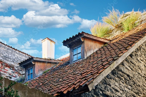 Fototapeta Historic stone building with ivy and red dormer window in Old European town. Old rustic stone facade with creeping ivy and a red wooden dormer window under a bright blue sky. 