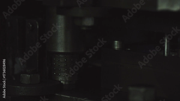 Fototapeta Dark view of a heavy industrial machine featuring various metallic mechanical components, including a textured cylinder and securing bolts, conveying a sense of manufacturing and internal workings