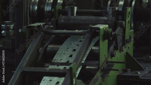 Fototapeta Metal strip feeds through automated punching press on factory production line, producing perforated sheet metal components in a precision metalworking operation within industrial plant