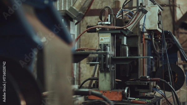 Fototapeta Industrial welding machine in specialized heavy industry workshop with electrical cables showing manufacturing process of various metal parts, representing automation, technology, and engineering