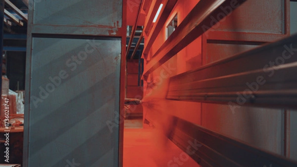 Fototapeta Metal profiles move along automated conveyor while machine applies vibrant reddish orange powder coat for durable, uniform industrial finishing and protection
