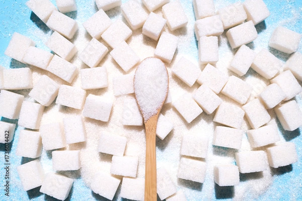 Fototapeta Scattered cubes of white refined sugar and a wooden spoon with granulated sugar on blue background top view flat lay. Concept of eating sweets, health and diabetes issue, sugar addiction
