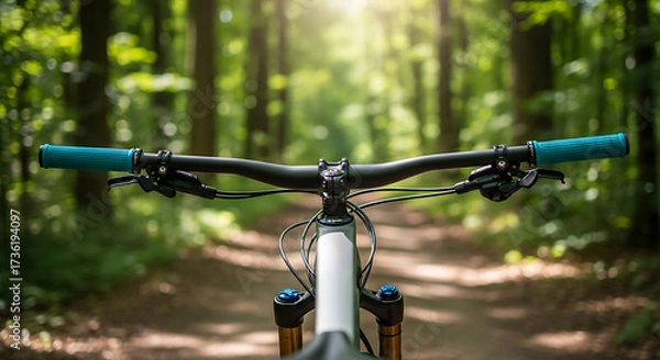 Fototapeta Close-up of a mountain bike handlebar with blue grips, on a forest trail, offering a first-person perspective of a cycling adventure.