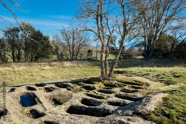 Fototapeta Ground-level view of the San Andres necropolis in Villarcayo, Burgos, Spain. The image shows medieval rock-cut tombs carved directly into stone, surrounded by natural vegetation and rural landscapes