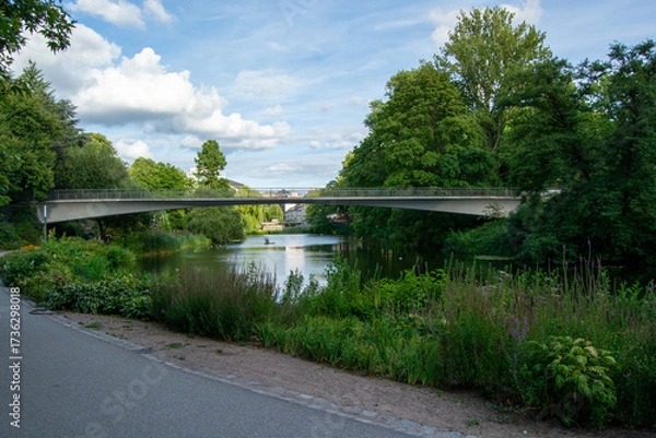 Fototapeta Modern bridge over a tranquil lake in a lush park