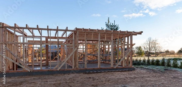 Fototapeta Wooden house frame construction on building site, sustainable architecture concept, eco friendly residential project, carpentry structure, outdoor housing development under clear blue sky background