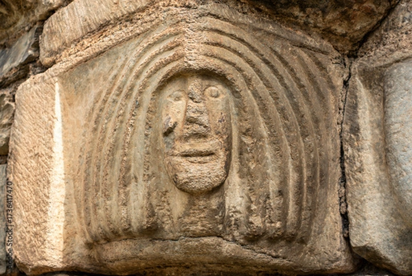 Fototapeta Close-up of a weathered stone capital from the Romanesque church of Sant Lliser d'Alós d'Isil, carved with a primitive, stylized human face. Catalonia, Spain.