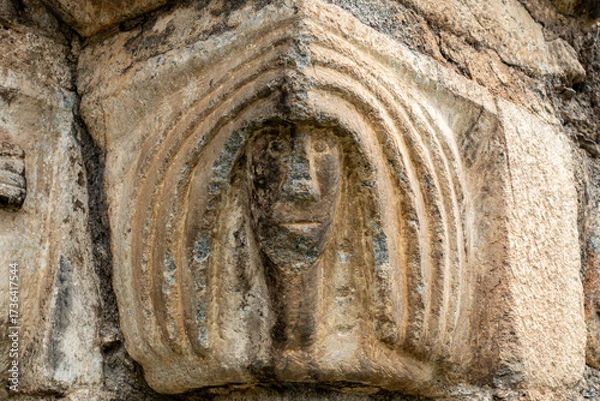 Fototapeta Close-up of a weathered Romanesque capital depicting a human face, an architectural detail of the historic Sant Lliser d'Alós d'Isil church in the Spanish Pyrenees. Catalonia