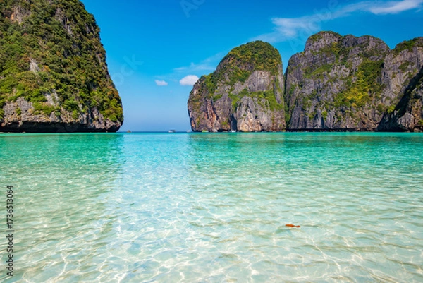 Fototapeta Maya Bay beach in Ko Phi Phi Leh, Krabi, Thailand featuring crystal clear turquoise water reflecting sunlight, surrounded by dramatic limestone karsts under a bright blue sky