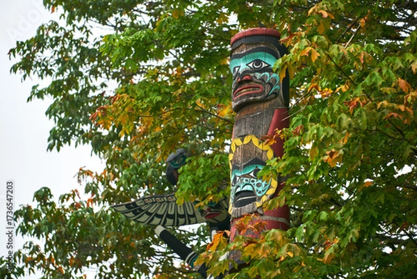 Fototapeta Stanley Park Totem in Autumn Trees. Stanley Park totem pole surrounded with autumn leaves, Vancouver, British Columbia, Canada.
