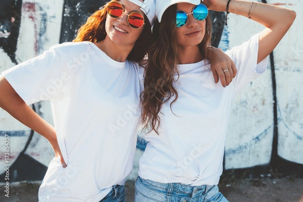 Obraz Modelki w prostym t-shircie i okularach przeciwsłonecznych pozują nad murem