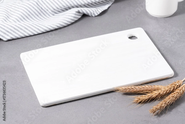 Fototapeta Wooden cutting board with fresh wheat stalks and striped cloth set on a gray tabletop