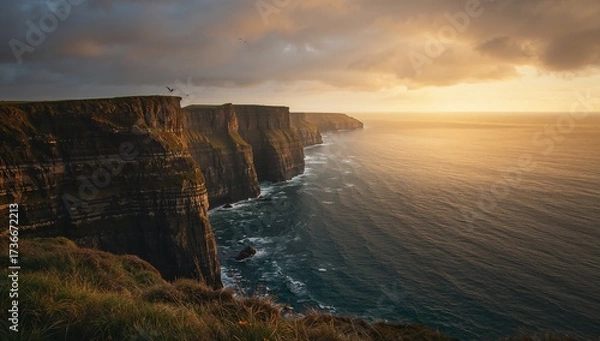 Fototapeta Dramatic cliffs and ocean coast with golden sunlight breaking through cloudy sky