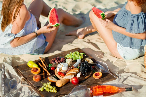 Fototapeta Two young female friends  on the sea shore enjoying  with watermelon.