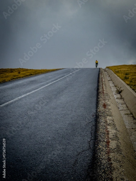 Fototapeta Cyclist climbs steep empty road into clouds