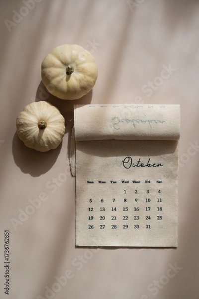 Fototapeta Linen fabric calendar with October month, decorative pumpkins, soft shadows, beige background, top view autumn aesthetic	