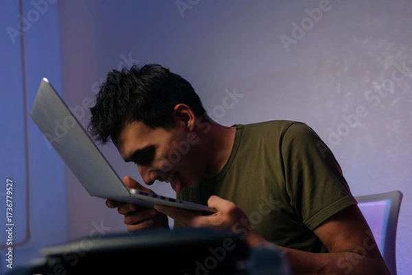Fototapeta Young programmer male showing extreme frustration by licking laptop after software crash, expressing desperation and anger in humorous way. Frustrated software developer licking laptop keyboard.