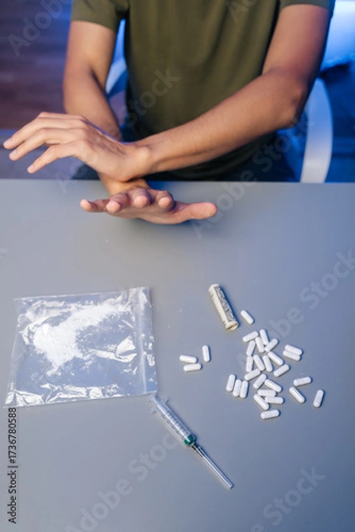 Fototapeta Vertical cropped shot of unrecognizable recovering drug user pushing away narcotics, surrounded by scattered medical tools and paraphernalia, representing personal battle against substance dependency.