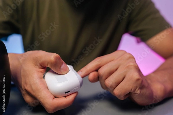 Fototapeta Cropped shot of unrecognizable man using portable electric nail clipper, filing nails on gray table while performing manicure at home using modern beauty tools for effortless grooming and self-care.