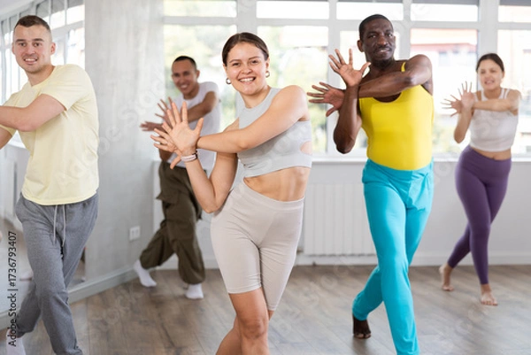 Fototapeta Positive young girl engaged in active dance together with other attendees of dancing courses