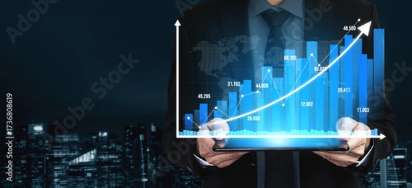 Fototapeta A professional businessman stands against a city skyline at night, holding a tablet that displays a blue growth graph, symbolizing success and analytics in finance. Tessel