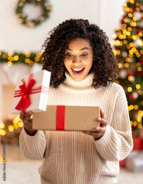 Fototapeta A person joyfully opening a gift box. The person displays a surprised and delighted expression while looking inside the box. Room is softly lit with blurred Christmas lights and holiday decorations.