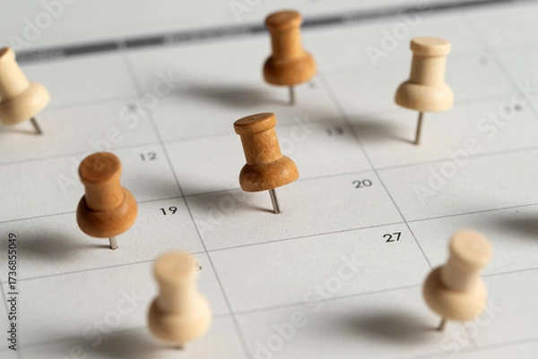 Fototapeta Wooden push pins marking important dates on a calendar, symbolizing planning, scheduling, reminders, and organization.