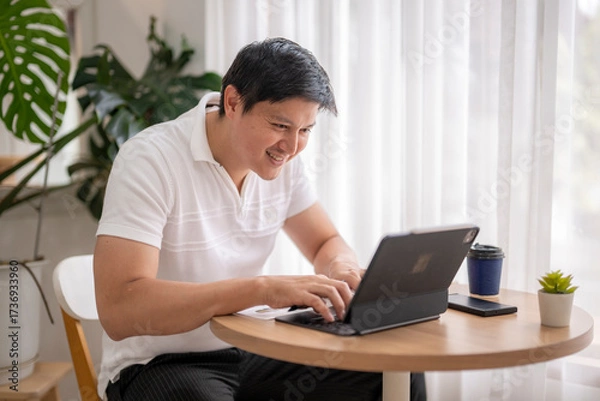 Fototapeta Asian freelancer working from home using tablet and keyboard at coffee table
