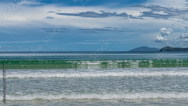 Fototapeta The waves of the turquoise ocean roll in rows to the shore, foaming. Reflection. Mountains on the horizon. Blue sky, clouds. A sunny summer day. Malaysia. Borneo. Kota Kinabalu.