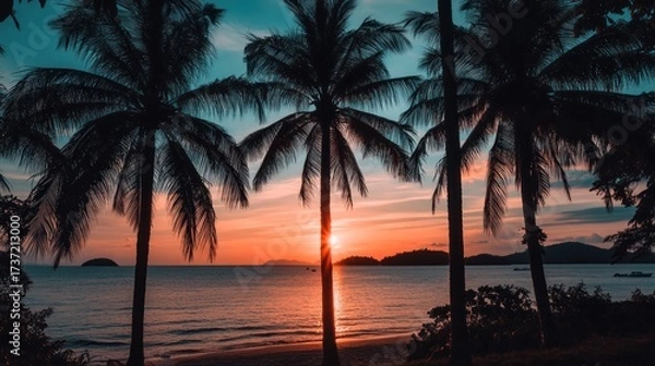 Fototapeta Silhouetted palm trees frame a vibrant sunset over a tranquil beach
