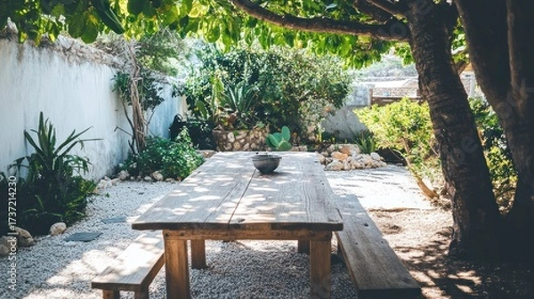 Fototapeta Wooden table and benches under a leafy tree in a sun-drenched garden patio