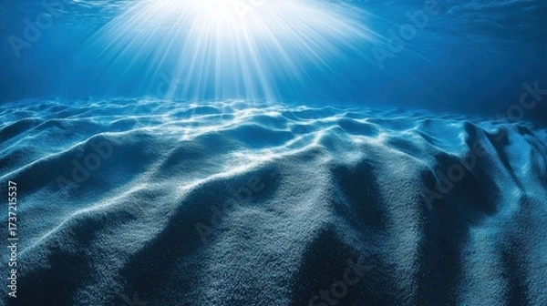 Fototapeta Sunbeams pierce the deep ocean floor, illuminating a textured, sandy seabed