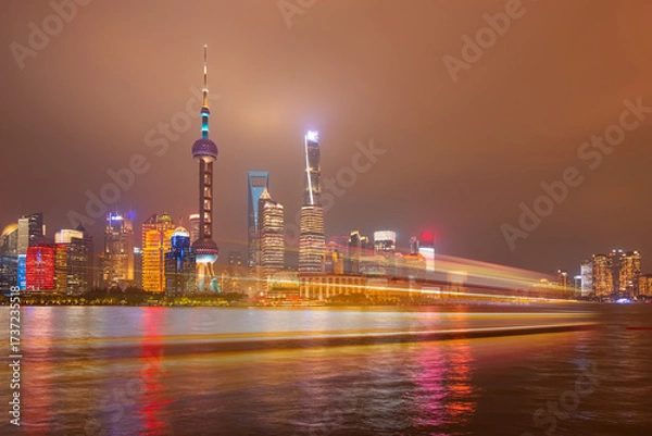 Fototapeta Shanghai colorful skyline with motion speed light of passing ferry in the foreground at night - Shanghai, China