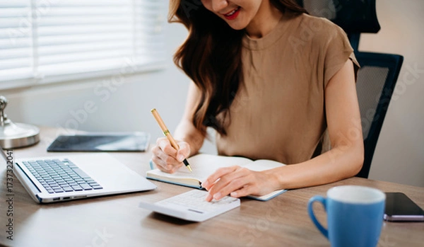 Fototapeta Confident businesswoman in office using calculator and laptop for accounting, finance, and tax report analysis
