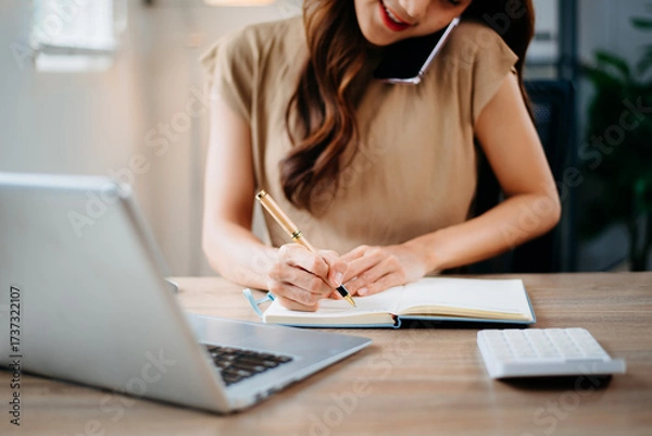 Fototapeta Closeup view of young professional businesswoman writing his idea concepts on notebook while working on his project at office