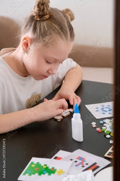 Obraz A girl makes a Christmas toy with her own hands from ceramic mosaic. Ceramic mosaic, DIY Christmas tree toy. Eco-friendly toy, educational activity for children.	