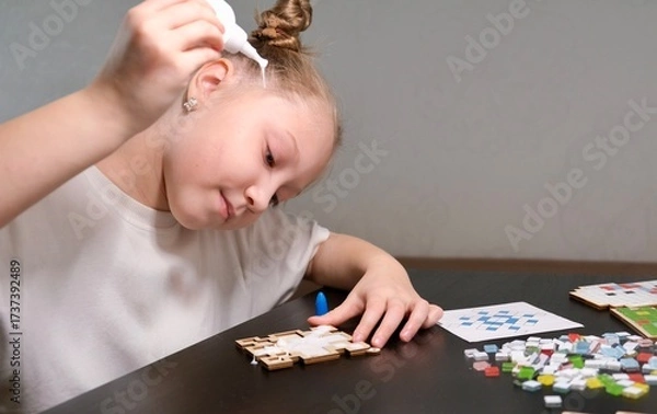 Obraz A girl makes a Christmas toy with her own hands from ceramic mosaic. Ceramic mosaic, DIY Christmas tree toy. Eco-friendly toy, educational activity for children.	