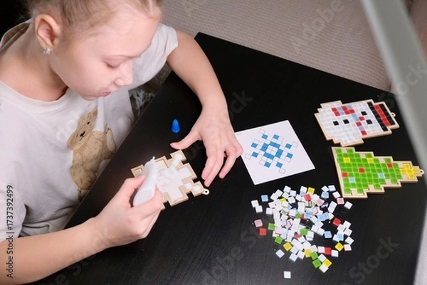 Obraz A girl makes a Christmas toy with her own hands from ceramic mosaic. Ceramic mosaic, DIY Christmas tree toy. Eco-friendly toy, educational activity for children.	