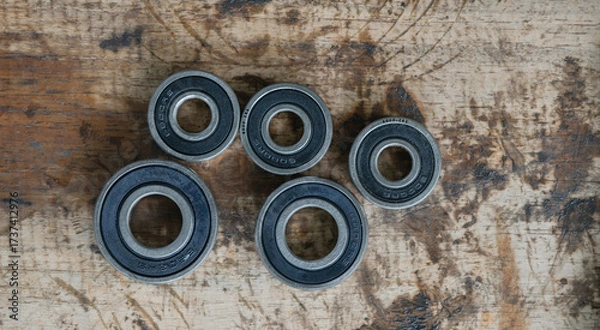Obraz A collection of metal ball bearings and bevel gears laid out on a worn wooden surface, likely in a workshop or repair setting. 