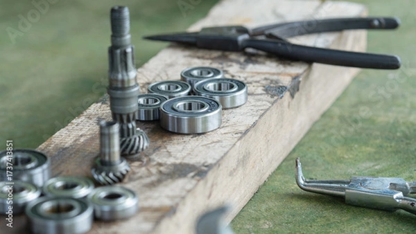 Obraz A collection of metal ball bearings and bevel gears laid out on a worn wooden surface, likely in a workshop or repair setting.