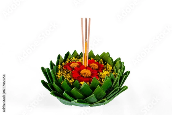 Fototapeta Banana leaf Krathong that have 3 incense sticks and candle decorates with red and yellow flowers for Loy Krathong festival isolated on white paper background.