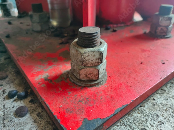 Fototapeta The image shows a bolt and two nuts, likely used to secure a component to a red metal base