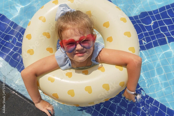 Fototapeta Portrait of a little girl floating with rubber ring in outdoor swimming pool 