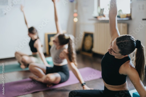 Fototapeta Three women performing yoga stretches together on mats in a sunny and inviting room, focusing on wellness, alignment, and community engagement while enjoying a balanced and peaceful environment.