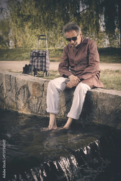 Fototapeta Senior citizen spending time alone in spring park with cart