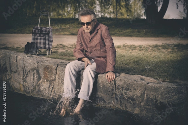 Fototapeta Senior citizen spending time alone in spring park with cart